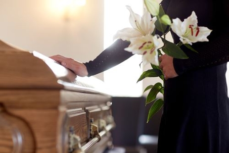 Woman placing hand on casket while holding flowers
