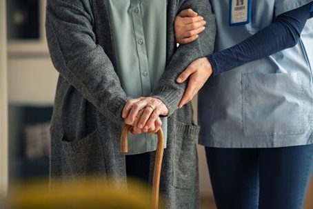 A cropped shot of nursing home staff member supporting arm of elderly resident holding walking cane.